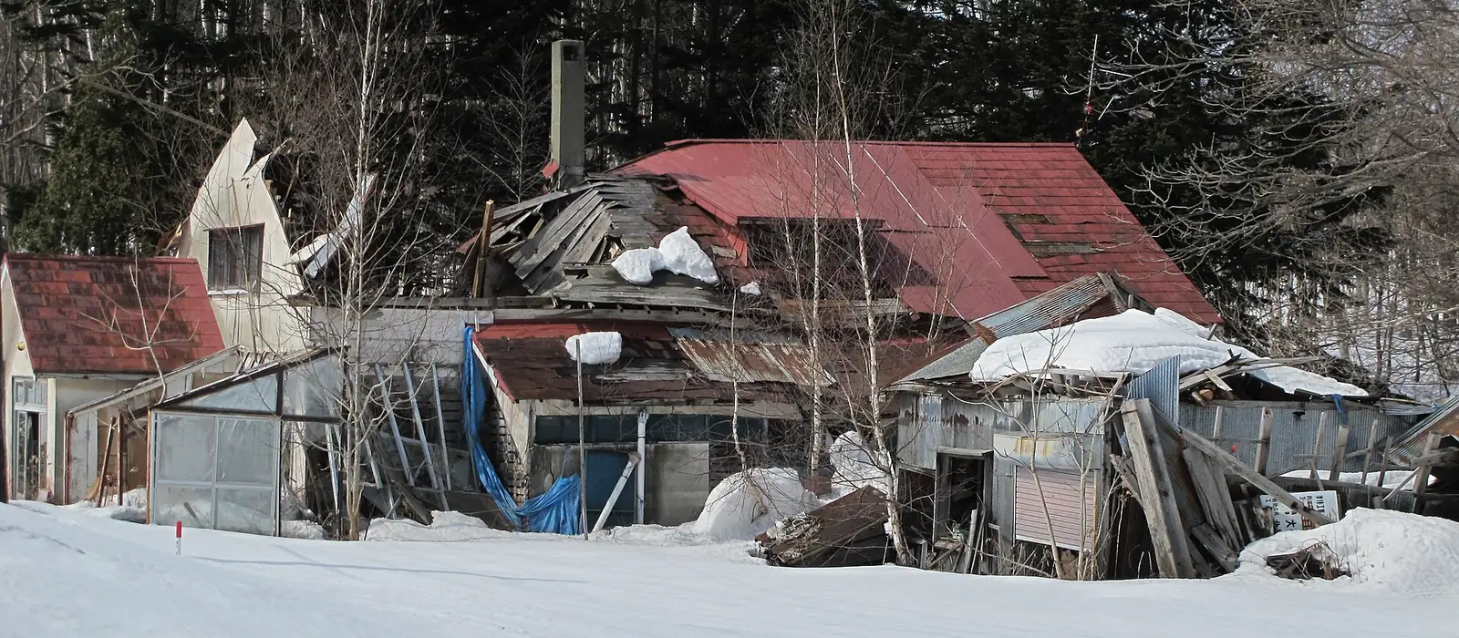 雪の重みで屋根が落ち、外壁と小屋が崩れたままの空き家（北海道）