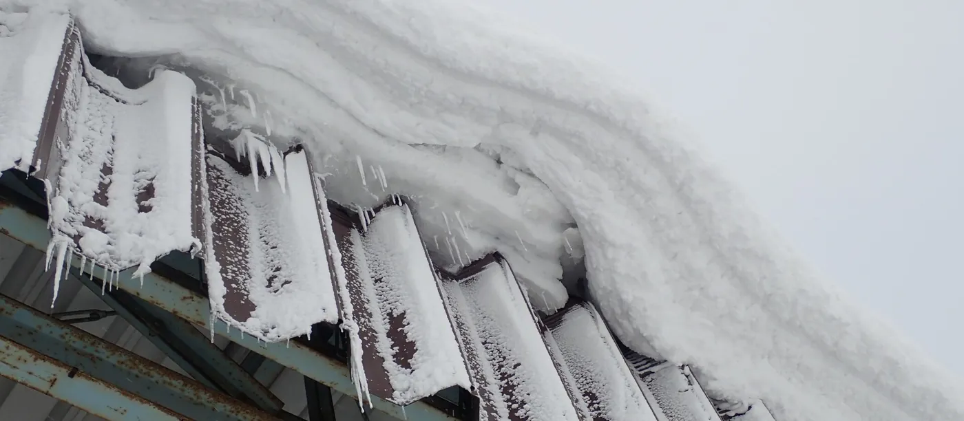 屋根の雪が軒先からせり出し、その下に氷柱が何本も下がった建物の軒（青森市）