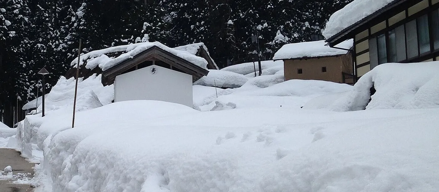 除雪した道の両脇に雪が積み上がり、小屋や家の屋根が雪をかぶった南砺市五箇山相倉の冬の集落