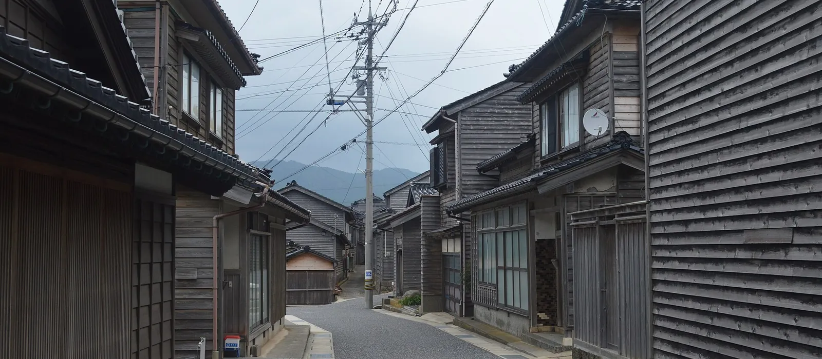 下見板張りの外壁と黒瓦の屋根の家が道の両側に並ぶ輪島市黒島地区の町並み